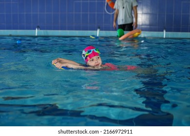 Small Preschooler Child Learns To Swim With Board In Pool. Swimming Lesson. Active Child Plays In Water. Kid In Mask And Goggles.