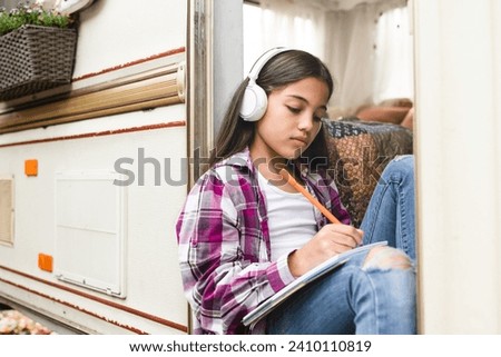 Small preteen learner girl daughter kid child listening to the music drawing doing homework while traveling by trailer camper van wheel motor home trailer