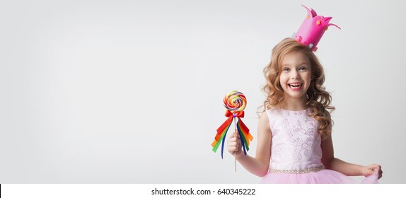 Small princess girl in crown holds a large spiral decorated lollipop candy - Powered by Shutterstock