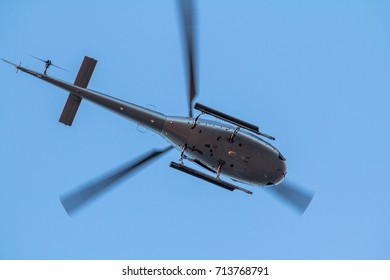 Small, private Helicopter while flying on blue clear sky, bottom view.