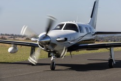 Small Private Single-engine White Piston Aircraft On Runway. Single-engine Piston Aircraft Taxied On The Runway. It Has A Propeller In Motion.