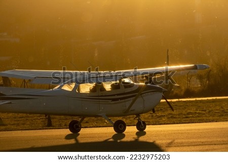 A small propeller plane rolling down the runway in backlight under a yellow sunset sun