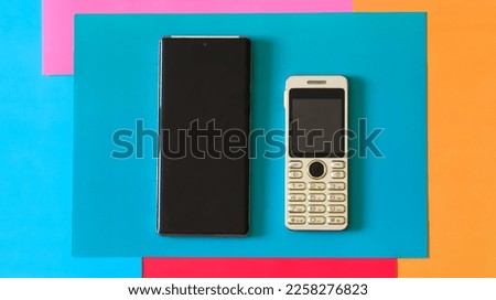 Small push-button mobile phone compared to a modern smartphone. Comparison of the sizes of mobile devices of different generations. Multicolored background. Close-up 