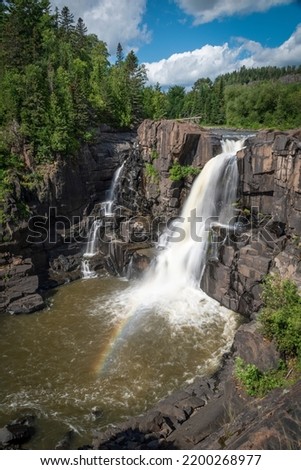 A small rainbow appears in front of High Falls in Pigeon River Provincial Park as the falls plunge down to a pool of water below.