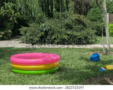 Small rainbow-colored kiddie pool on the grass by a countryside cottage. Instant backyard water fun for a hot day