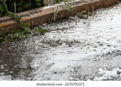 Small raindrops falling into big puddle on asphalt road. Rain drops splashing on reflective water surface. Summer rainy time. Concept of tranquility scene. Flood on heavy raining day.