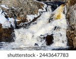 A small rapidly flowing waterfall in winter. There is a bit of ice around the waterfall. Fast shutter to freeze the action.