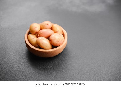 Small, raw potatoes are piled inside a wooden bowl on a dark background.
