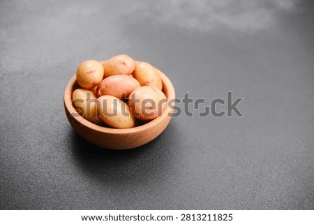 Small, raw potatoes are piled inside a wooden bowl on a dark background.