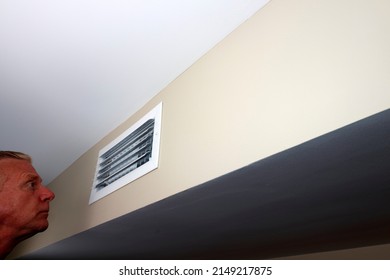 Small rectangle air vent furnace duct on a wall being examined by an adult caucasian man inside a home. Home HVAC air vent being inspected by an adult white male to make sure all is clean and flowing