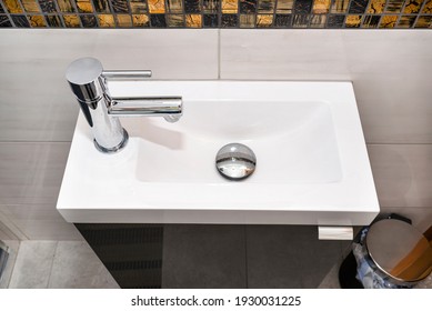 A small rectangular sink with a silver tap on the left in a tiled bathroom.
