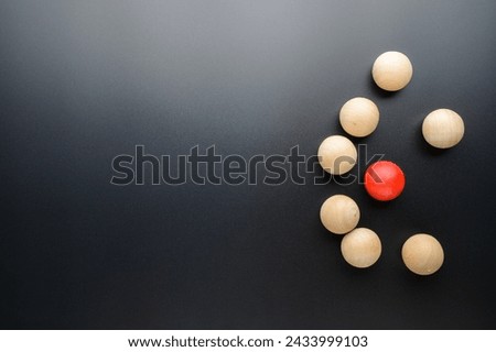 Small red ball is under siege of many wooden balls on black background, small business in competition, and enciclement, or niche, and different concept
