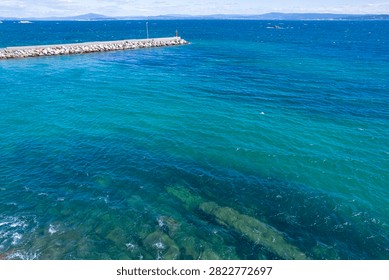 Small red beacon standing at the end of a rocky breakwater in the middle of the clear ocean