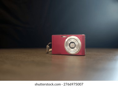 A small red compact digital camera sits on a wooden table
