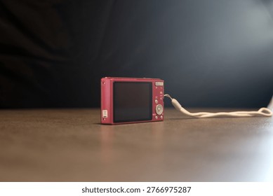A small red compact digital camera sits on a wooden table