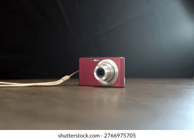 A small red compact digital camera sits on a wooden table