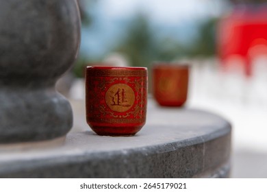 A small red cup is placed in front of the altar of worship, the cup is decorated with intricate traditional Chinese motifs in gold, a similar cup is visible in the background with a blurred effect