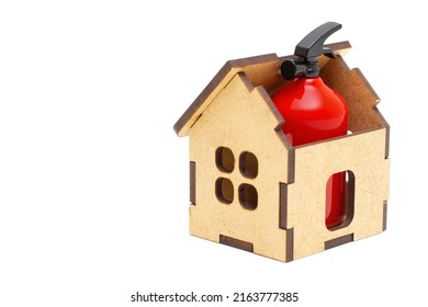 Small Red Fire Extinguisher Placed Inside A Toy Wooden House Isolated On White Background. Home Fire Safety And Prevention Measures.