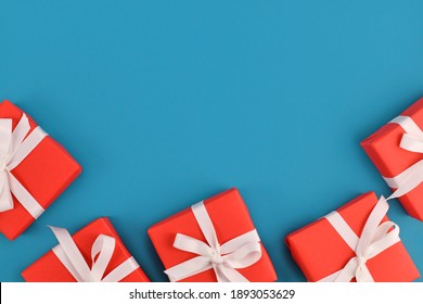 Small red gift boxes with white ribbons at bottom of blue background with empty copy space