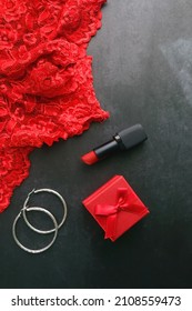 Small red giftbox, red lipstick, silver earrings and lace underpants. Valentine's Day objects on dark background. Flat lay.