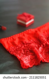 Small red giftbox, red lipstick, silver earrings and lace underpants. Valentine's Day objects on dark background. Selective focus.