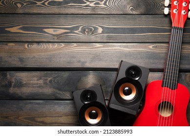 A Small Red Guitar And Musical Speaker On The Wooden Flat Lay Table Background With Copy Space.