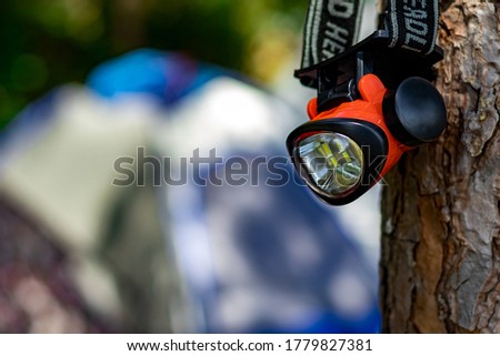 small red head lamp for camping hanging on the tree with unfocused camping tent. travel and camp theme