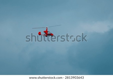 Small red helicopter flying in cloudy sky