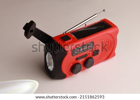 Small red portable radio rechargeable with solar panels or manually with a crank. Flashlight included
