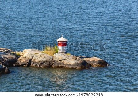 Small red and white lighthouse on island near Stockholm, capital of Sweden. Overhead view of technical building for navigating ships on sunny day. Summer boat trip in Scandinavia.
