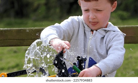 Small redhead boy playing and puddling in water in the garden