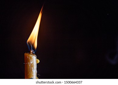 A small remainder of a candle burning out against a dark background.