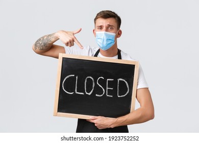 Small Retail Business Owners, Covid-19 And Social Distancing Concept. Disappointed And Sad Salesman In Medical Mask, Barista Showing Closed Sign, Inform Clients Restaurant Not Working