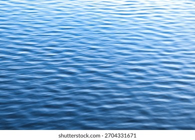 Small ripples create patterns on the surface of the calm water. The water color shifts from a lighter to a darker blue in the distance. Copy ad text space
