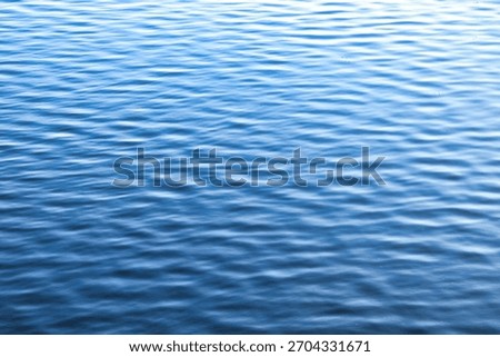 Small ripples create patterns on the surface of the calm water. The water color shifts from a lighter to a darker blue in the distance. Copy ad text space