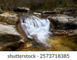 Small river cascade with smooth effect due to long exposure between trees in autumn