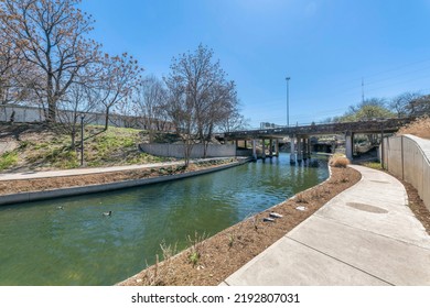 Small river with concrete walkways on the side heading to a bridge at San Antonio, Texas. Empty riverside with walkways near the bridge at the front against the electrical post and sky at the back.