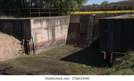 Small River Dam Of Sideway Channel Of Vah River, Slovakia With Visible Inflow Part, Grate For Filtering Dirt And Dirty Water. Spring Season, Rapeseed Field In Background. 