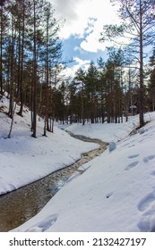 A small river flows through the forest through deep snow next to a wooden house