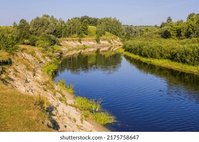 a small river with green and steep bank on a summer day