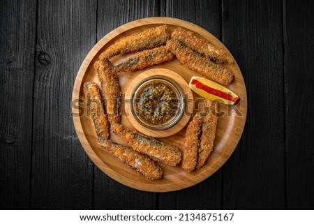 Small river or sea fish fried in batter with paprika and lemon. Snack for Oktoberfest beer or vodka. Wooden plate on black boards.