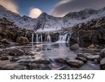 Small river with waterfall in snowy landscape with winter Cullins mountains in the background, Carbost, Portree, Isle of Skye, Scotland, United Kingdom, Europe