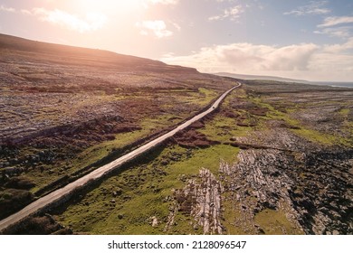 Small road by a mountain in Burren, Ireland. Wild Atlantic way. Beautiful scenery with rough stone surface and green grass hill. Nobody, Warm sunny day. Travel and tourism area.
