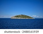 Small rocky island emerging from the deep blue sea on sunny summer day.