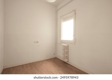 Small room featuring a single window letting in bright natural light, a radiator beneath the window, and white walls, offering a simplistic and clean environment. - Powered by Shutterstock