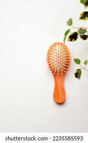 Small round wooden natural hair comb on a white table. Ficus greenery in the frame. Hair care. Simple minimalistic light photo. Empty space for text, design. Isolated organic eco cosmetic product. - Shutterstock ID 2235585593