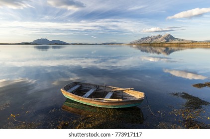 Small Rowing Boat. Mountains On Horizon Reflecting On Water Surface. Photographed In Helgeland, Norway. 