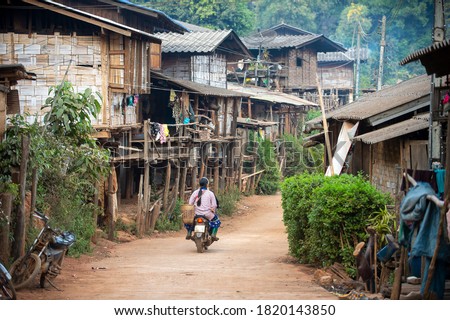 A small rural village, a hill tribe village in Chiang Mai Thailand, houses made of wood and bamboo, and a dirt road with a motorbike.