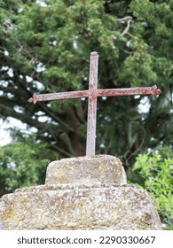 Small rusted iron cross on top of a small stone monument (