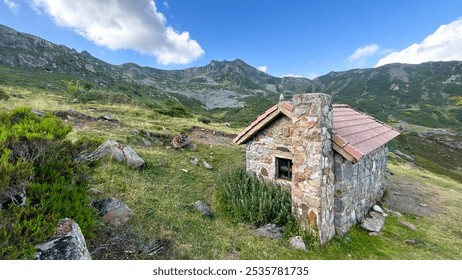 A small rustic stone cabin sits alone in a picturesque mountain landscape, surrounded by grassy hills and rocky terrain under a bright blue sky. Ideal for rural living, solitude, and nature-themed ima - Powered by Shutterstock